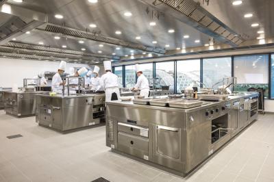 Cuisiniers en tenue blanche travaillant dans une grande cuisine professionnelle équipée d'appareils en inox.