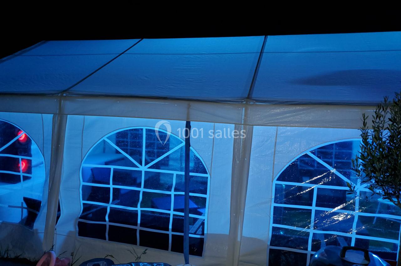 Tente blanche éclairée en bleu la nuit, avec des fenêtres en plastique transparent montrant l'intérieur faiblement visible.