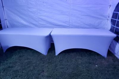 Grande tente blanche rectangulaire installée sur un parking, entourée de végétation et de barrières de sécurité.