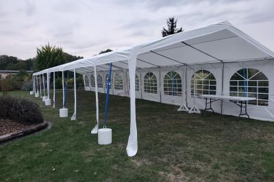Grande tente blanche avec fenêtres en arc, installée sur un parking entouré de végétation.