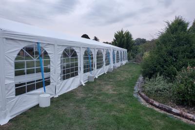 Grande tente blanche avec fenêtres en arc, installée sur un parking entouré de végétation.