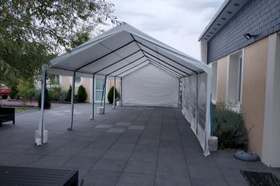 Grande tente blanche avec fenêtres en arc, installée sur un parking entouré de végétation.