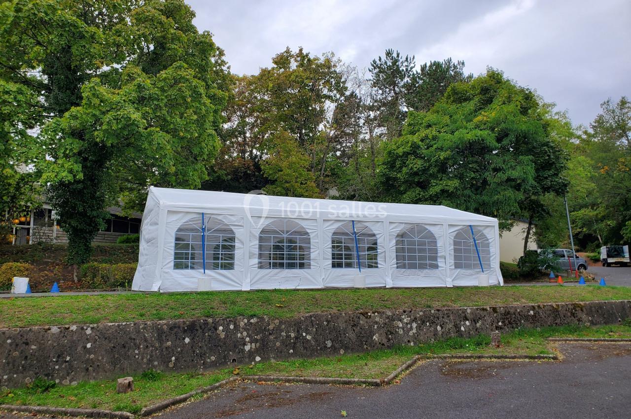 Tente blanche rectangulaire installée sur une pelouse, entourée d'arbres et d'un mur bas en pierre.