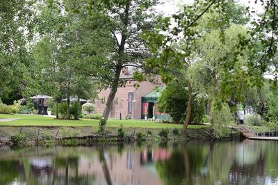Vue d'un parc verdoyant avec des arbres, une pelouse et une rivière au premier plan, sous un ciel clair.
