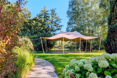 Tente éclairée par des guirlandes lumineuses dans un jardin verdoyant au crépuscule.