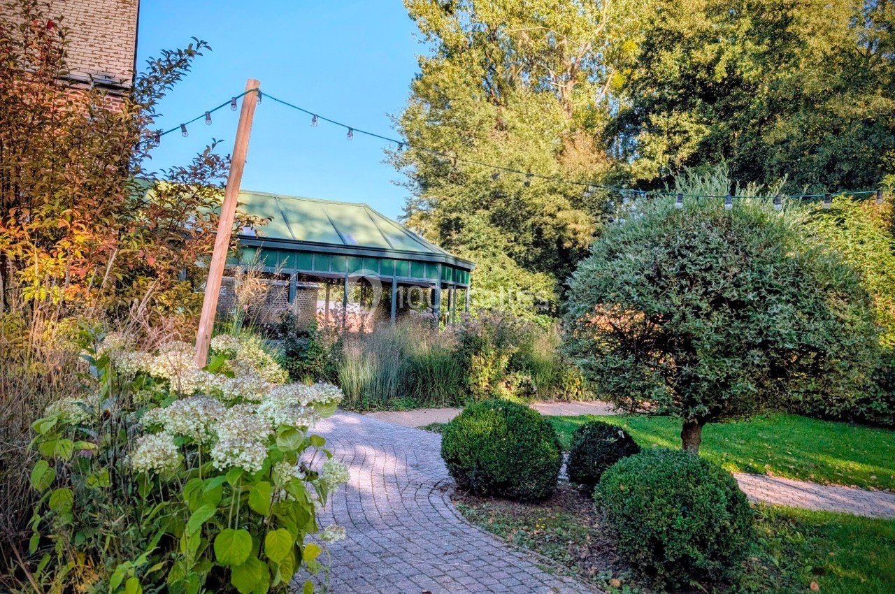 Chemin pavé serpentant dans un jardin verdoyant avec une serre en arrière-plan sous un ciel dégagé.