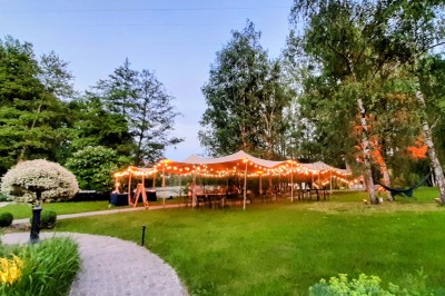 Tente éclairée par des guirlandes lumineuses dans un jardin verdoyant au crépuscule.