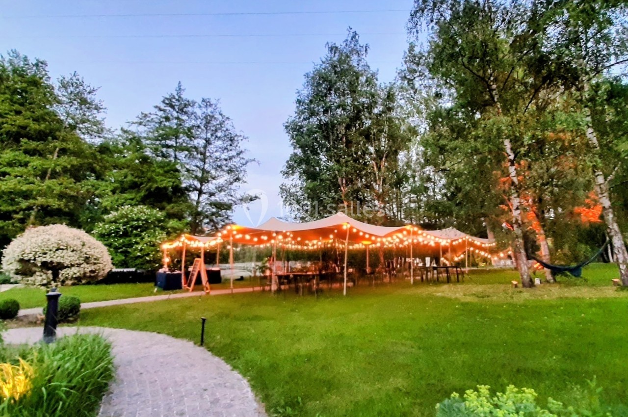 Tente éclairée par des guirlandes lumineuses dans un jardin verdoyant au crépuscule.