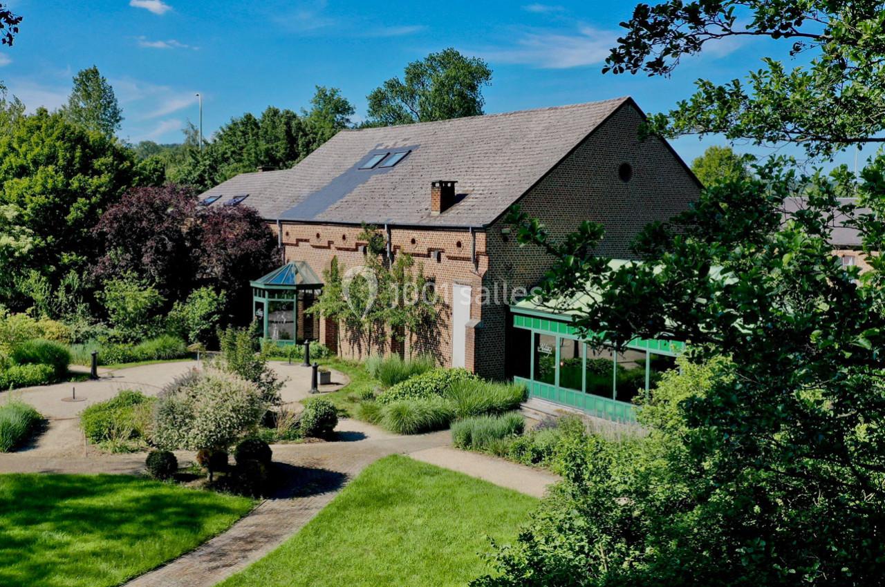 Bâtiment en briques entouré de jardins verdoyants avec allées gravillonnées, sous un ciel bleu dégagé.