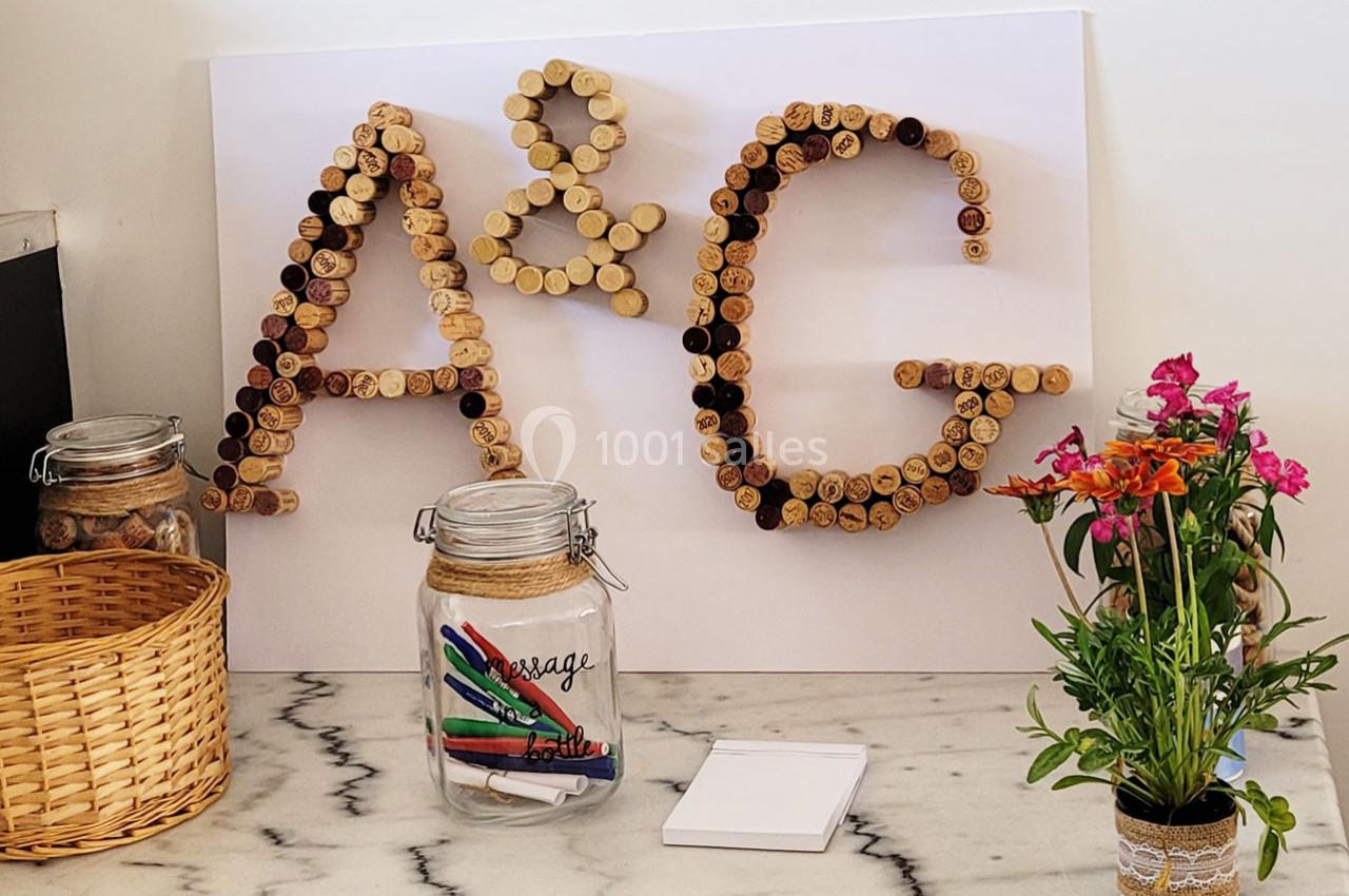 Lettres ’A & G’ formées avec des bouchons en liège, entourées de pots en verre, d'un panier et d'un vase de fleurs.