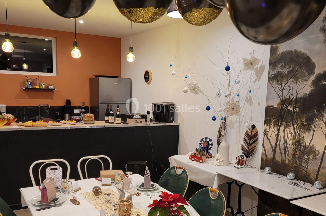 Salle décorée pour une fête avec ballons noirs, tables dressées, guirlandes et un arbre blanc orné de décorations.