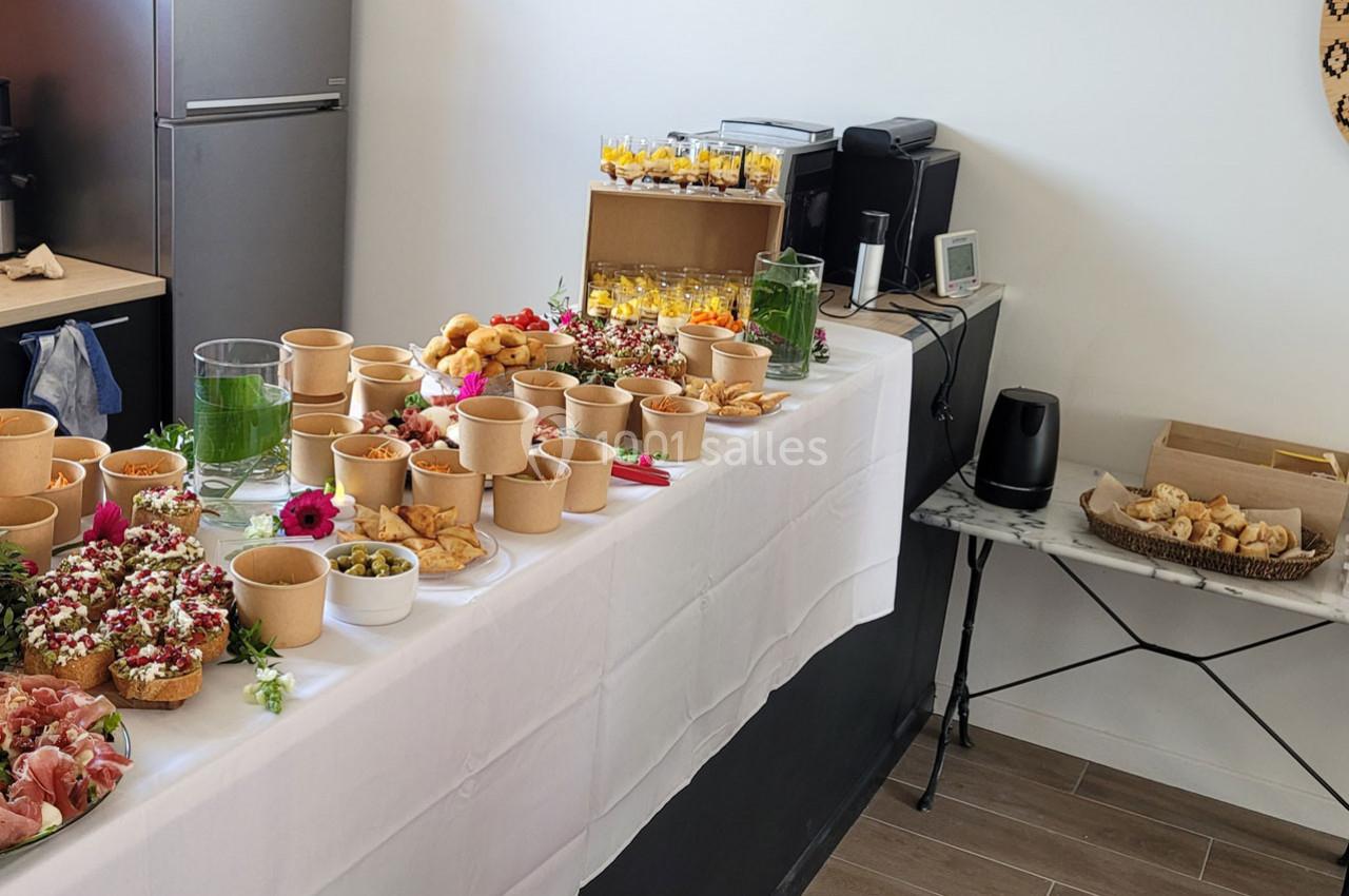 Buffet avec divers plats, verrines, pains et garnitures disposés sur une table blanche dans une salle lumineuse.