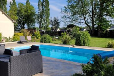 Jardin en soirée avec des arbustes fleuris, éclairé par des lampes au sol, entouré d'arbres et de végétation.
