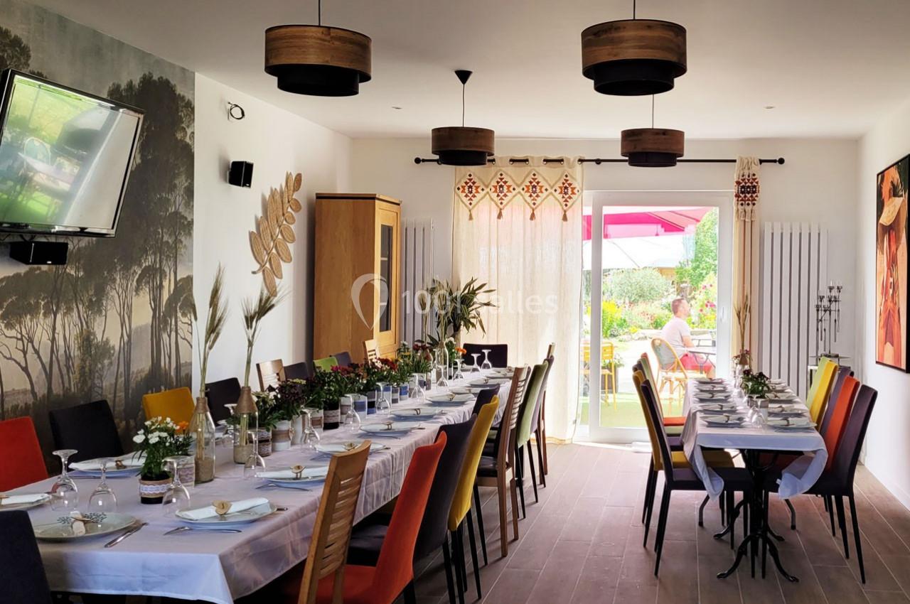 Salle à manger lumineuse avec une grande table dressée, chaises colorées et vue sur un jardin ensoleillé.