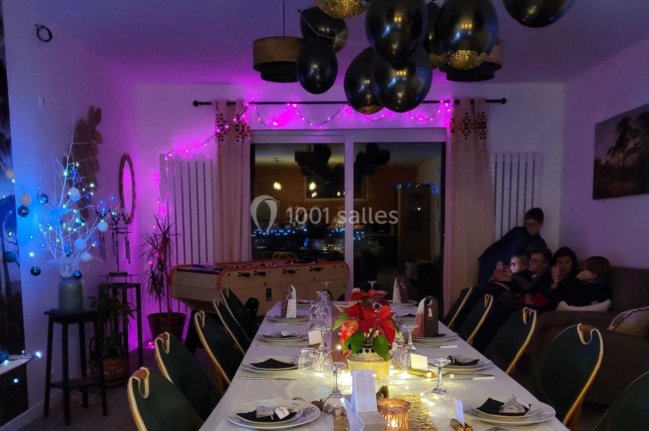 Salle à manger décorée pour une fête avec table dressée, guirlandes lumineuses et ballons noirs suspendus.