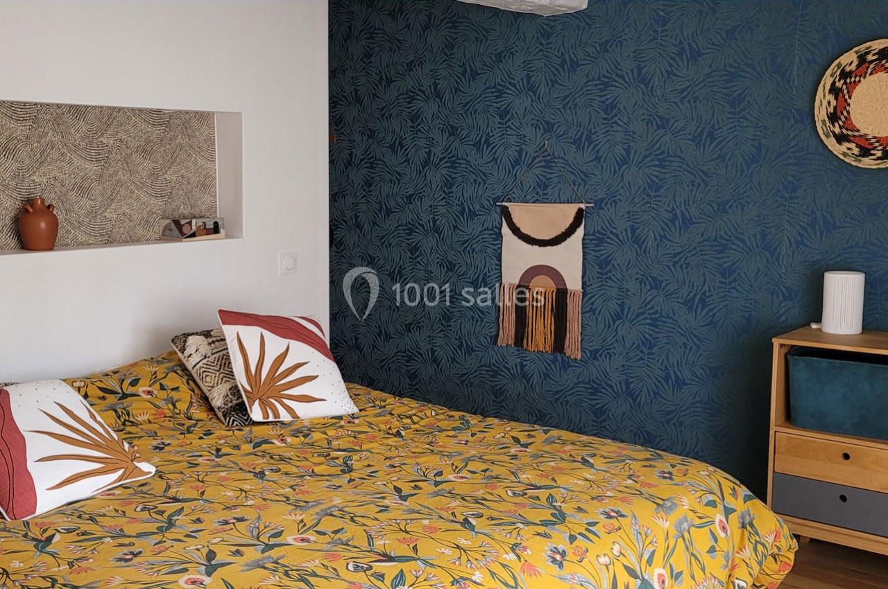 Chambre avec un lit à motif floral, mur bleu texturé, étagère intégrée et décoration murale en tissu et osier.