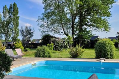 Jardin en soirée avec des arbustes fleuris, éclairé par des lampes au sol, entouré d'arbres et de végétation.