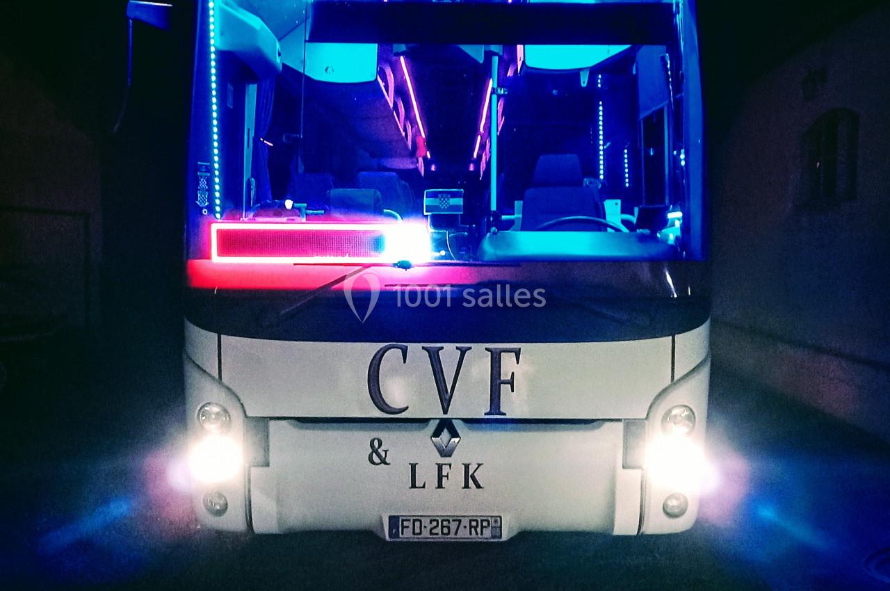 Autobus illuminé par des néons colorés, stationné de nuit avec une enseigne visible sur le pare-brise.