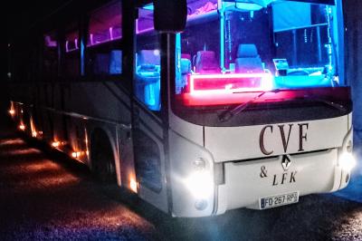 Intérieur d'un autocar avec sièges rouges, éclairage tamisé et allée centrale recouverte d'un tapis rouge.