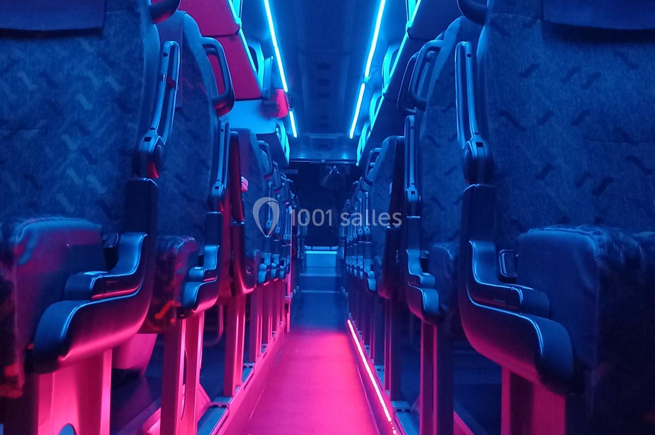 Allée centrale d'un bus vide avec éclairage intérieur bleu et rose, sièges alignés de chaque côté.