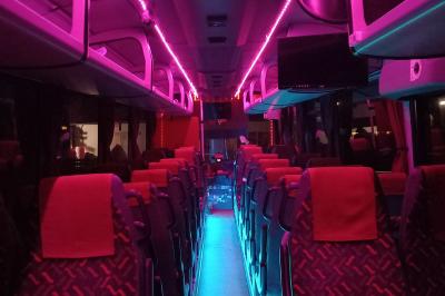 Intérieur d'un autocar avec sièges rouges, éclairage tamisé et allée centrale recouverte d'un tapis rouge.