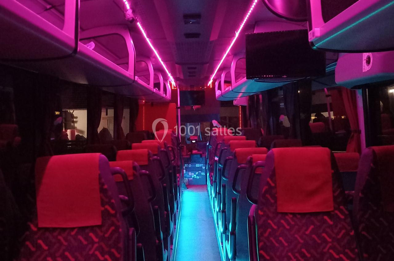 Intérieur d'un bus avec éclairage LED rose et bleu, rangées de sièges vides et tablettes rabattables.