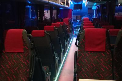 Intérieur d'un autocar avec sièges rouges, éclairage tamisé et allée centrale recouverte d'un tapis rouge.