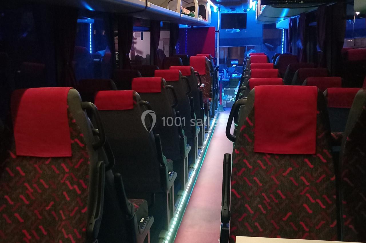 Intérieur d'un autocar vide avec sièges rouges et noirs, éclairage tamisé et allée centrale illuminée.