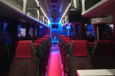 Intérieur d'un autocar avec sièges rouges, éclairage tamisé et allée centrale recouverte d'un tapis rouge.