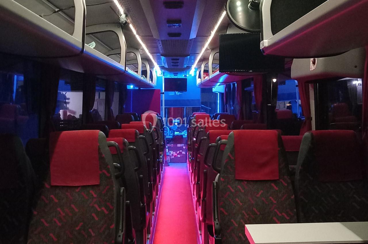 Intérieur d'un autocar avec sièges rouges, éclairage tamisé et allée centrale recouverte d'un tapis rouge.