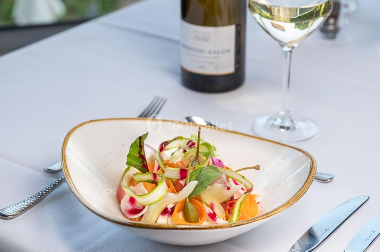 Assiette de salade colorée avec légumes frais, servie sur une table dressée avec verre de vin blanc et bouteille.