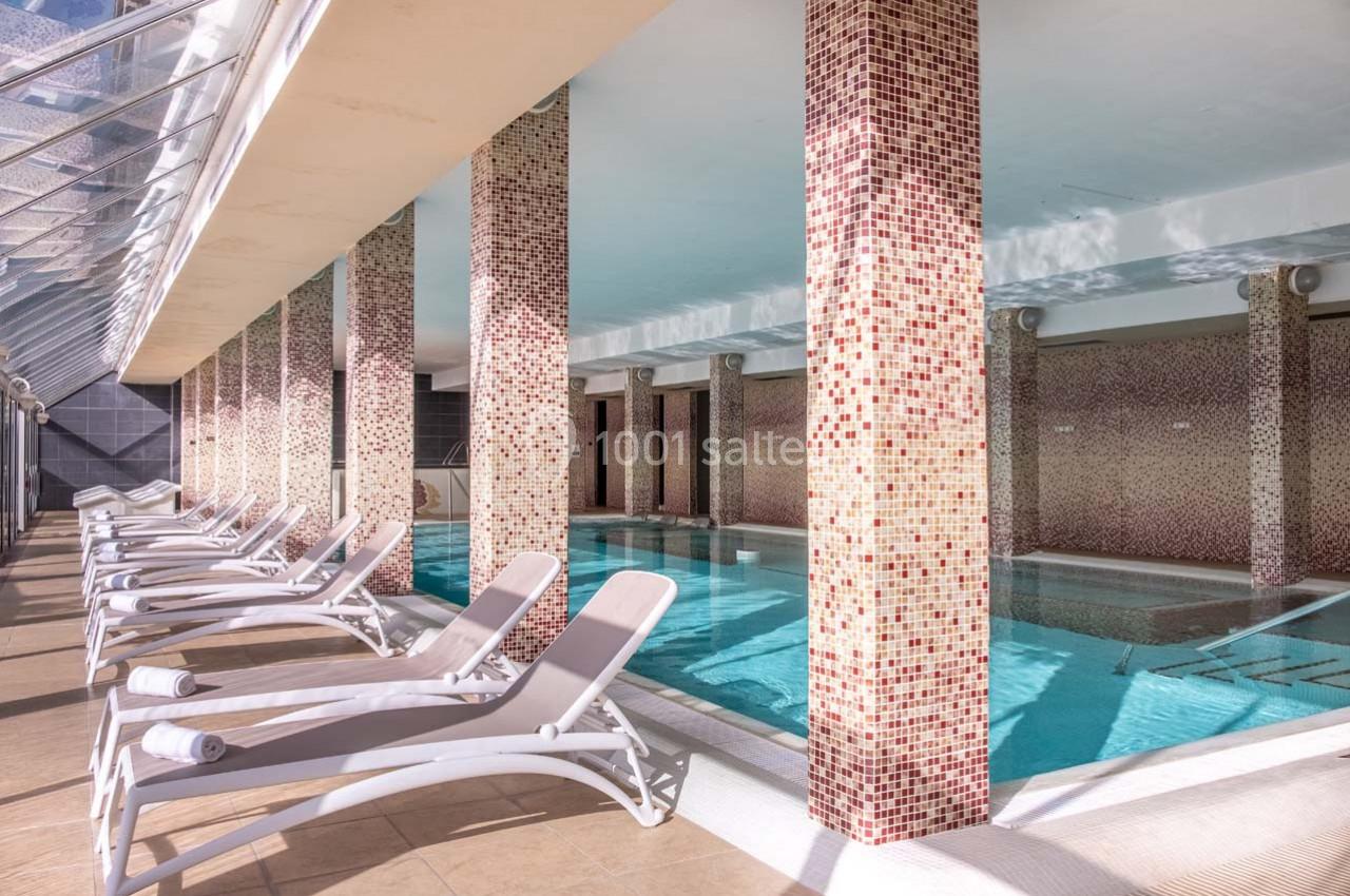 Piscine intérieure avec colonnes décoratives et transats alignés le long d'un sol carrelé clair.