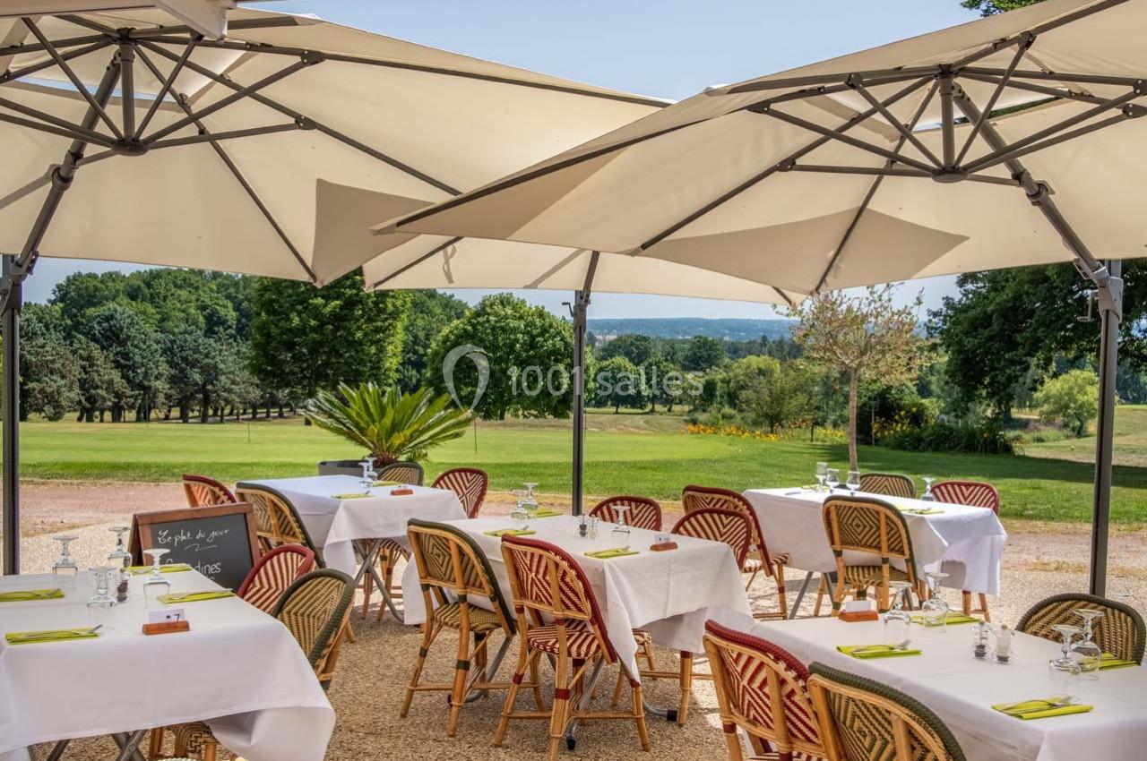 Terrasse d'un restaurant avec tables dressées sous des parasols, offrant une vue sur un paysage verdoyant.
