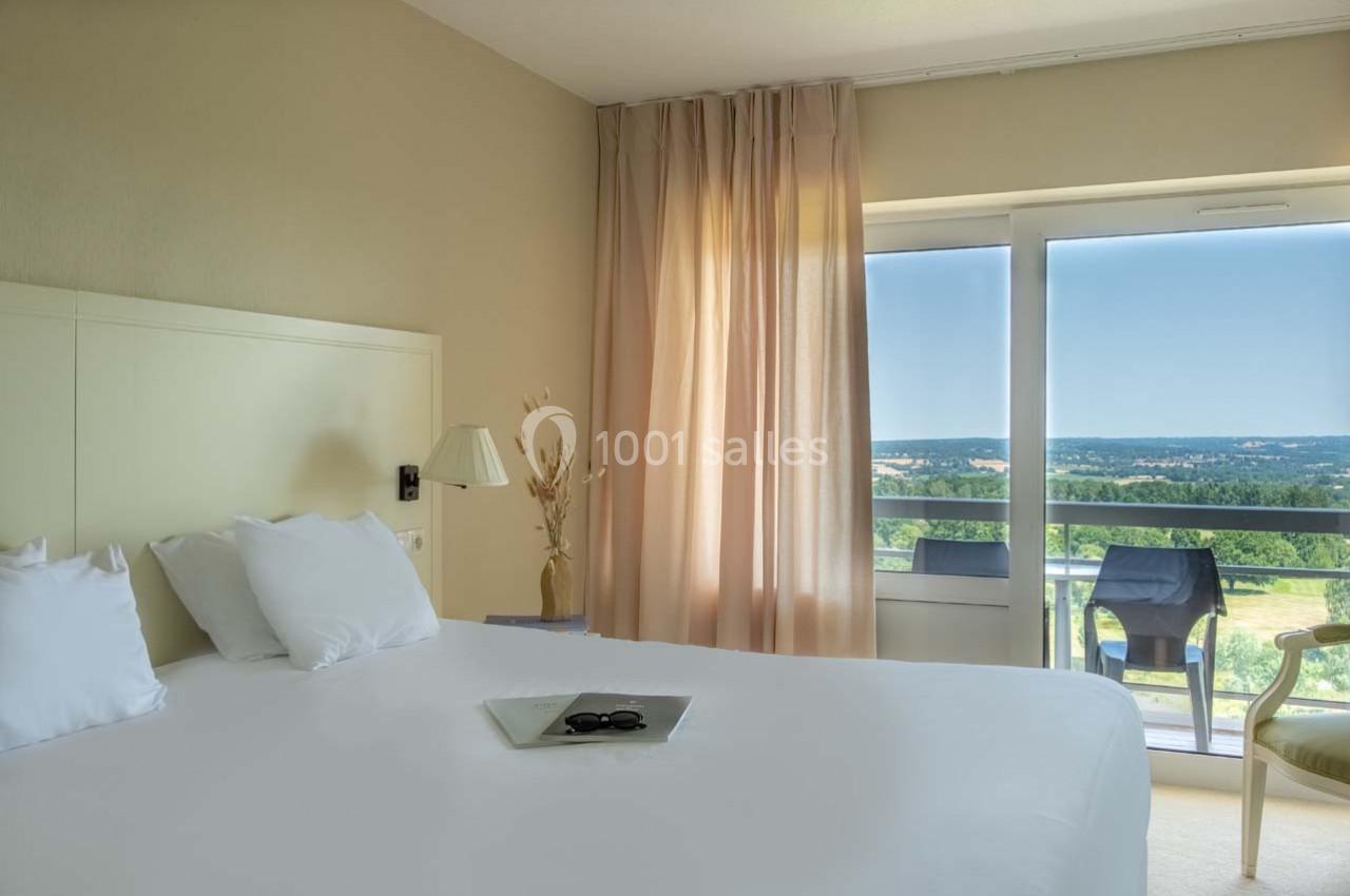 Chambre lumineuse avec lit double, rideaux beiges, grande fenêtre donnant sur un balcon et une vue dégagée.