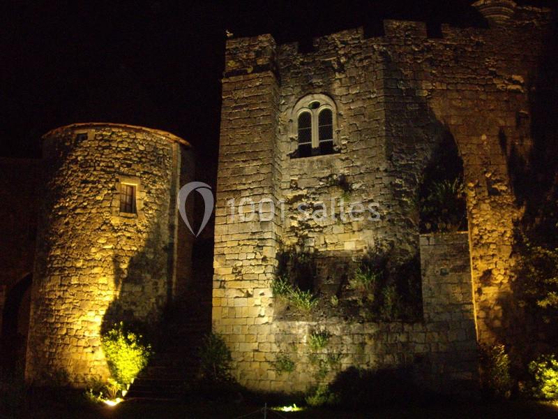 Vue nocturne d'un château en pierre éclairé par des projecteurs, mettant en valeur ses murs et ses fenêtres.