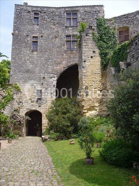 Façade en pierre d'un bâtiment ancien avec une arche, entourée de verdure et d'un chemin pavé.