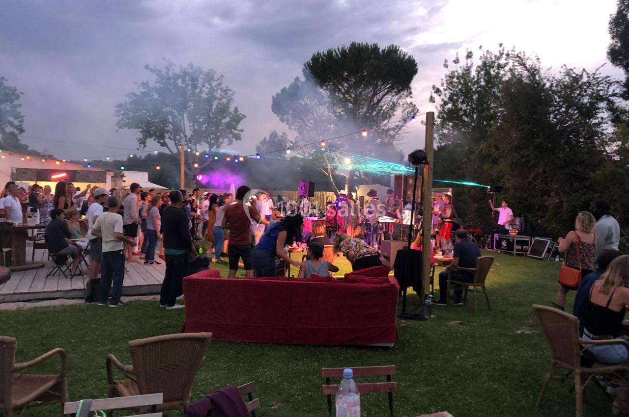 Groupe de personnes réunies dans un jardin en soirée, avec musique, éclairages colorés et ambiance festive.