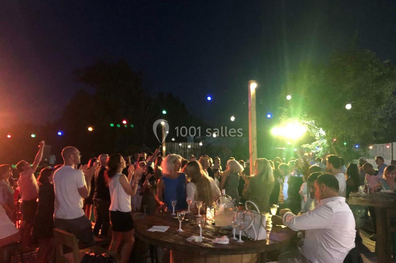 Groupe de personnes debout et assises lors d'une soirée en plein air, éclairée par des guirlandes lumineuses.