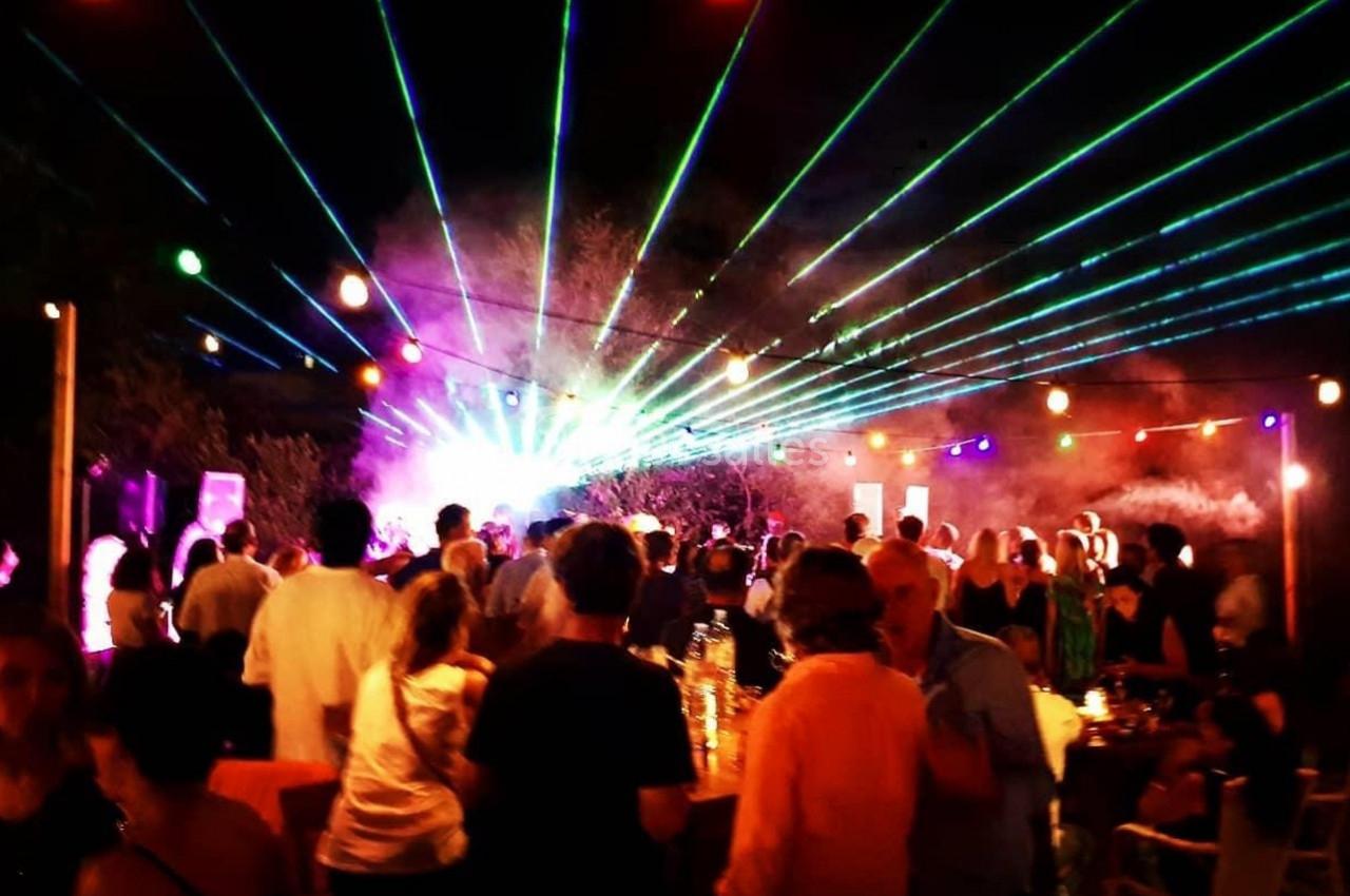 Foule rassemblée en soirée en plein air avec des jeux de lumières colorées et des lasers dans une ambiance festive.