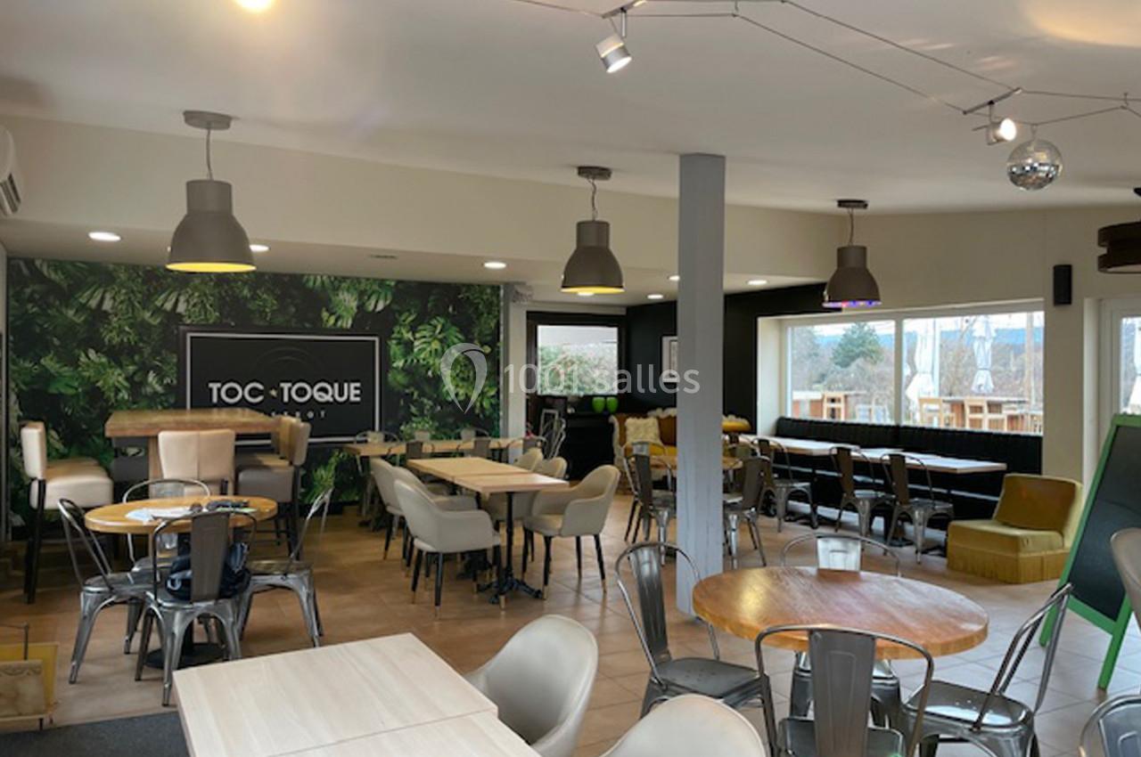 Salle de restaurant lumineuse avec tables en bois, chaises variées et mur décoré de motifs végétaux.