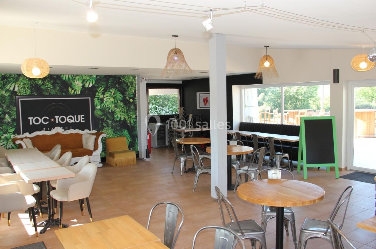 Salle de restaurant lumineuse avec tables en bois, chaises variées et mur décoré de motifs végétaux.