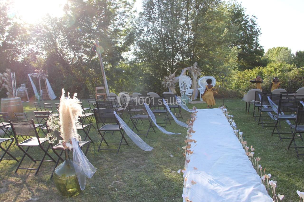 Allée décorée pour une cérémonie en plein air, avec chaises alignées, fleurs et arche au fond dans un cadre naturel.