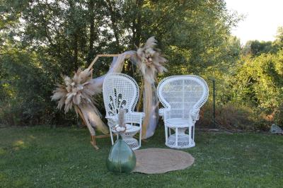Deux fauteuils en osier blanc entourés de décorations florales et de voilages, installés sur une pelouse verdoyante.