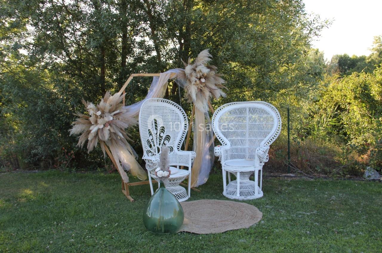 Deux fauteuils en osier blanc entourés de décorations florales et de voilages, installés sur une pelouse verdoyante.
