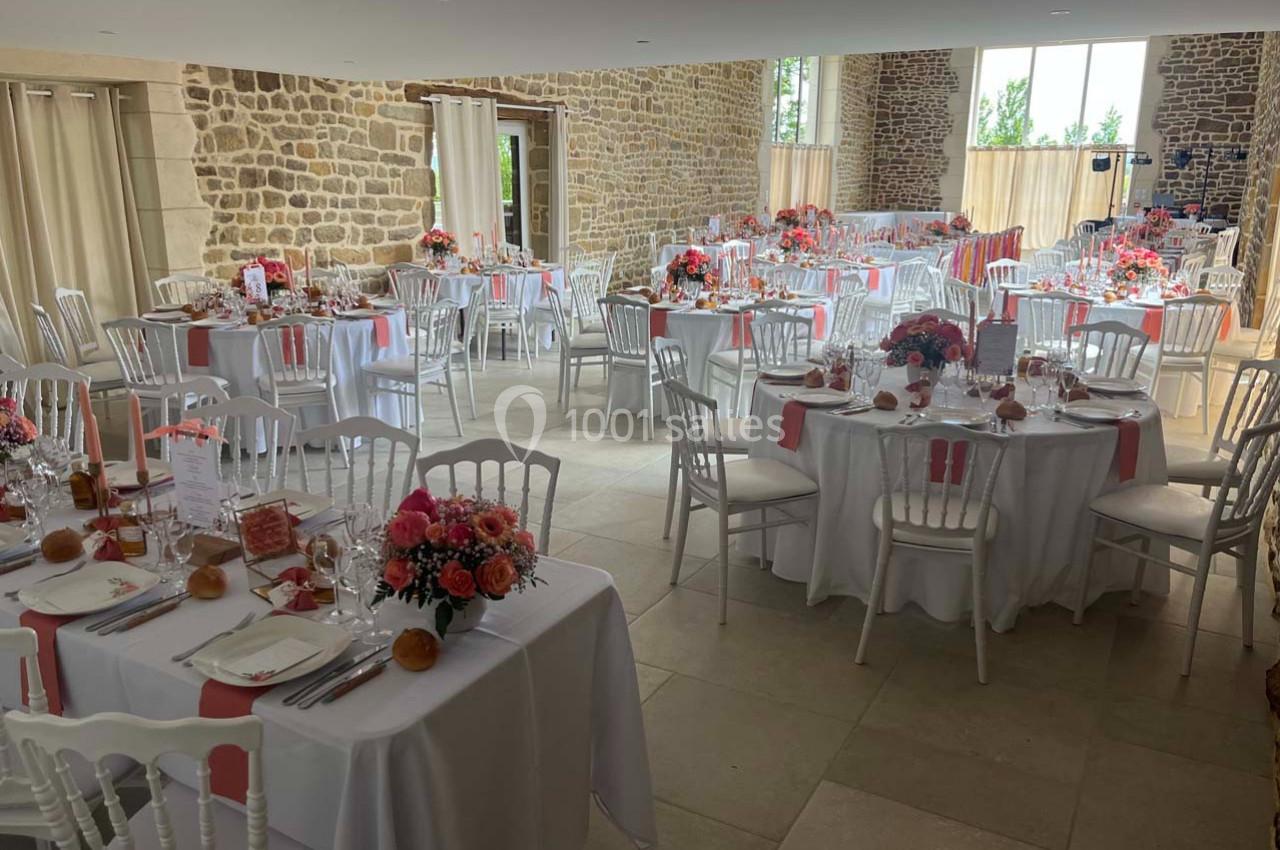 Salle de réception décorée avec des tables rondes, nappes blanches, chaises blanches et arrangements floraux colorés.