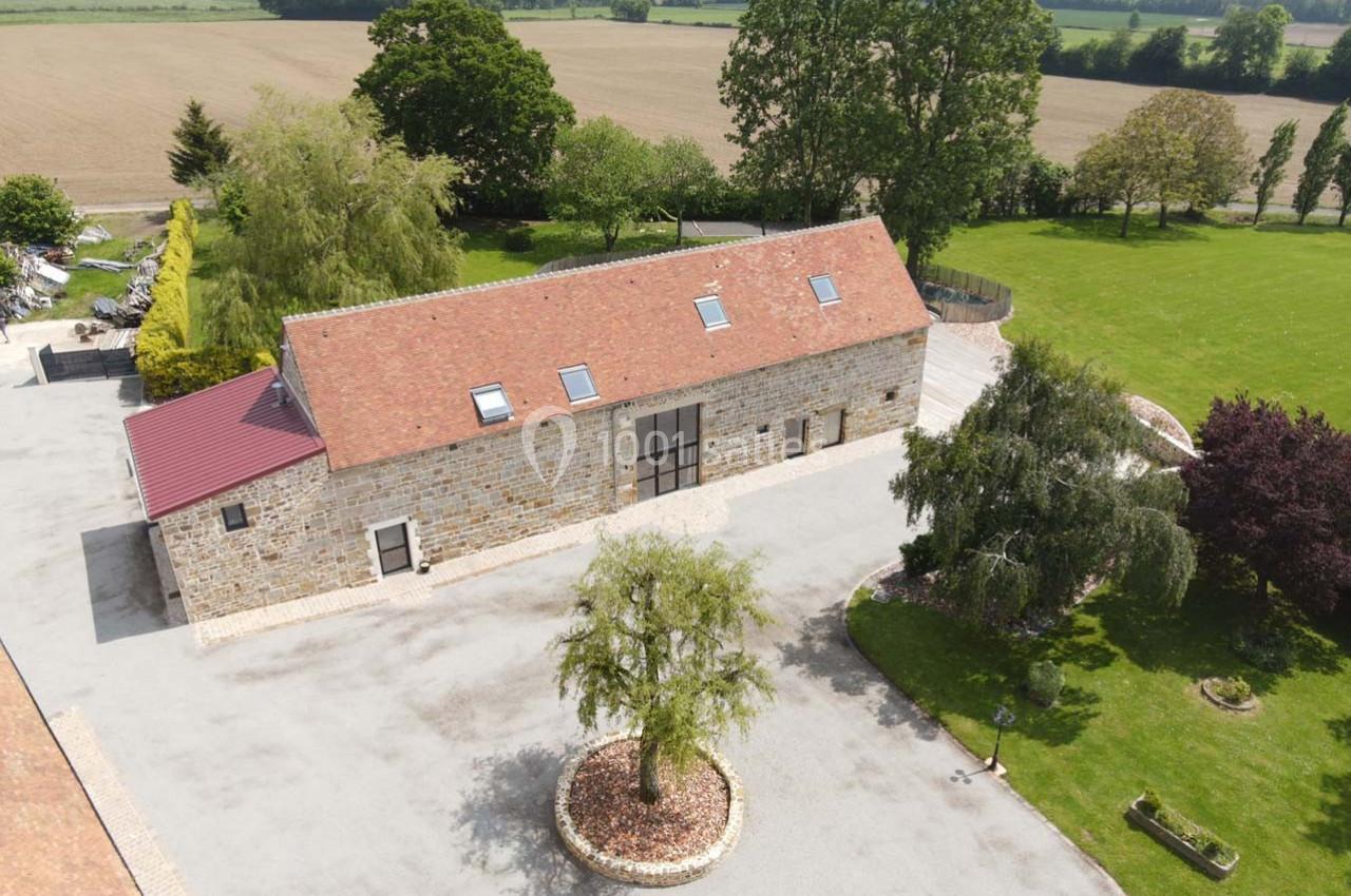 Vue aérienne d'une grange rénovée en pierre avec toit en tuiles, entourée d'arbres et d'espaces verts.