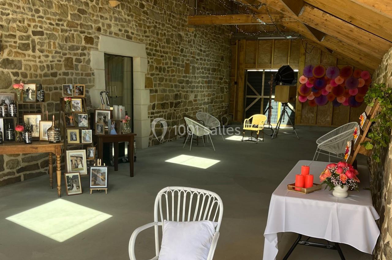Salle en pierre avec décoration festive, chaises blanches, table ornée de bougies et mur décoré de fleurs en papier.