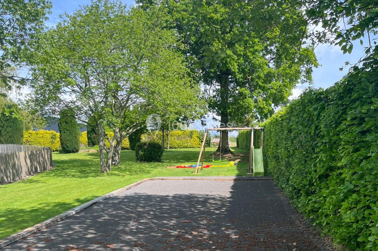 Allée ombragée menant à un jardin avec des arbres, une pelouse et une aire de jeux comprenant un toboggan.