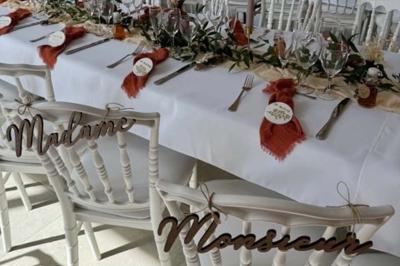 Salle en pierre décorée avec des cadres photo, des chaises blanches et des bougies sur une table.