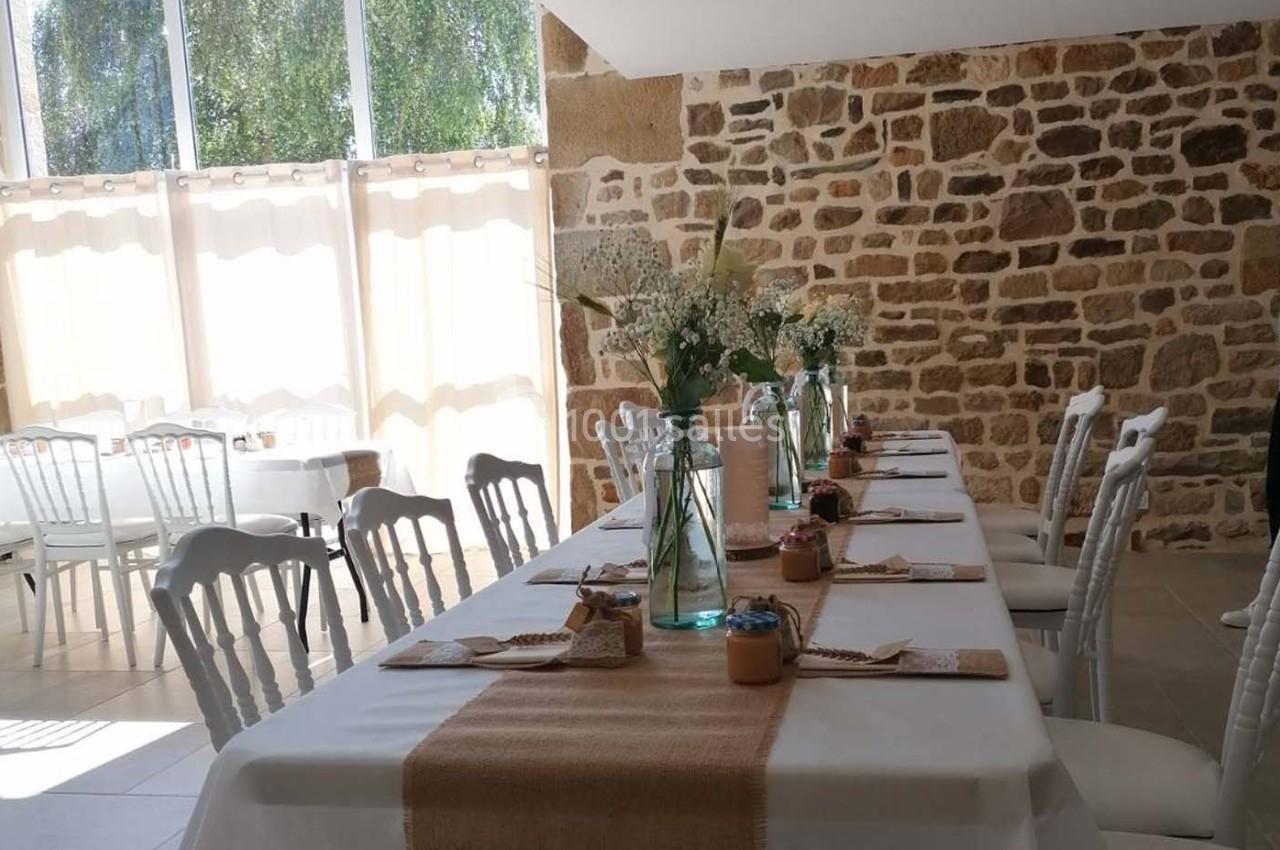 Salle lumineuse avec tables décorées de nappes blanches, chemins de table en toile de jute et bouquets de fleurs.